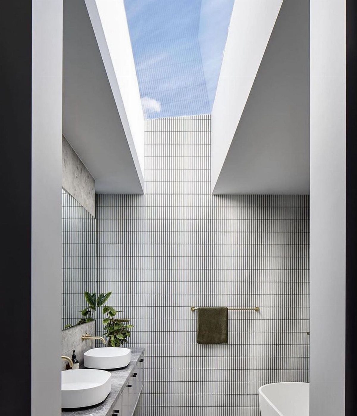 Modern bathroom with white vertical tiles and a rectangular skylight showing blue sky.