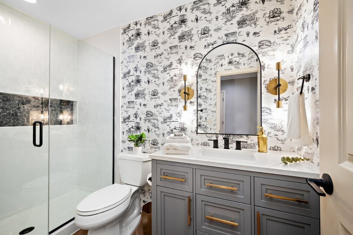 Bathroom with black and white illustrative wallpaper, grey vanity, and arched mirror.