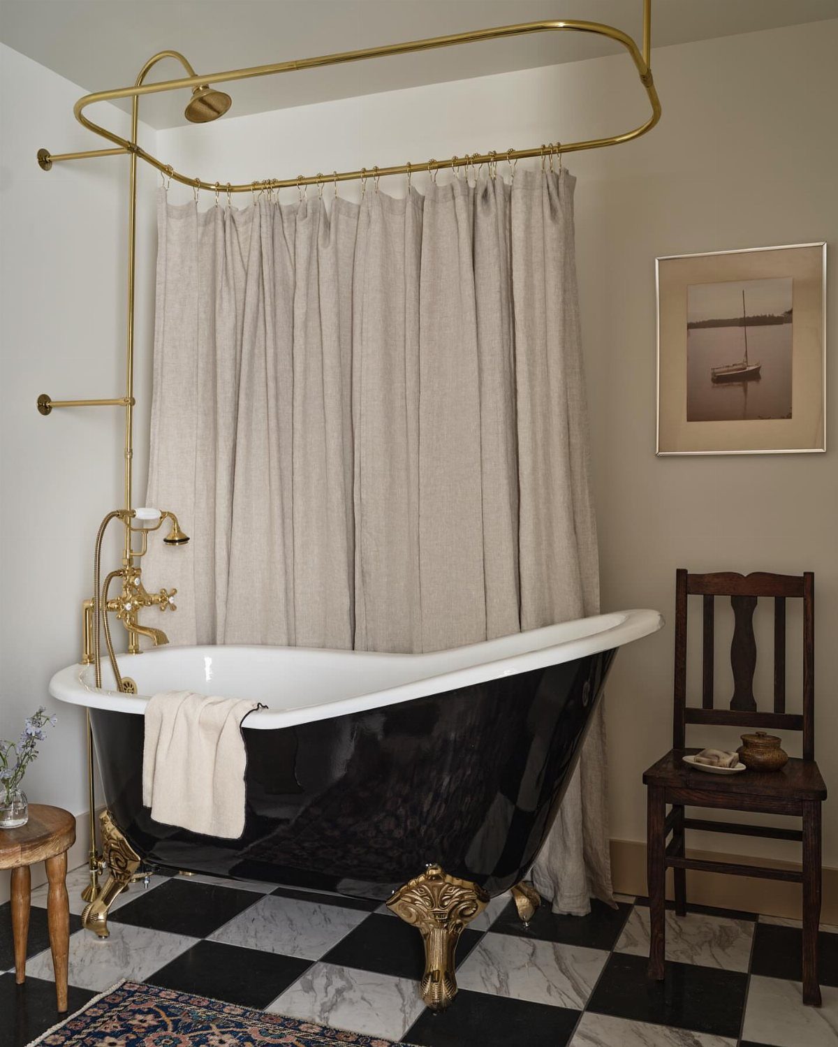 Black clawfoot bathtub with gold feet on a black and white checkered floor.