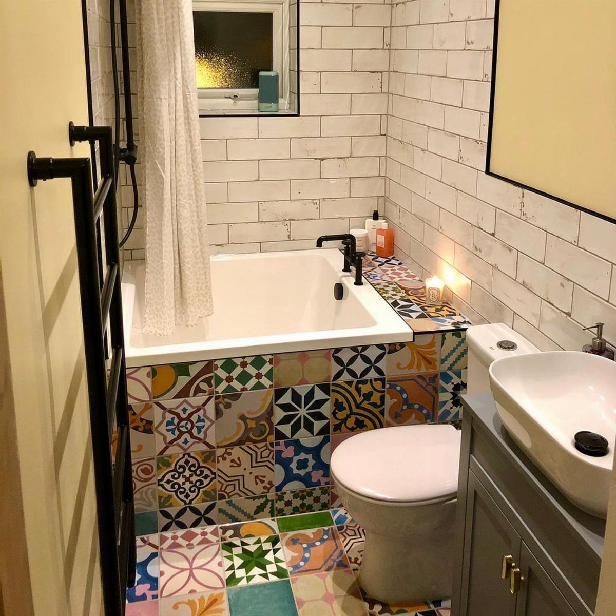 Compact white bathtub with colorful patterned tiles in a small, bright bathroom.