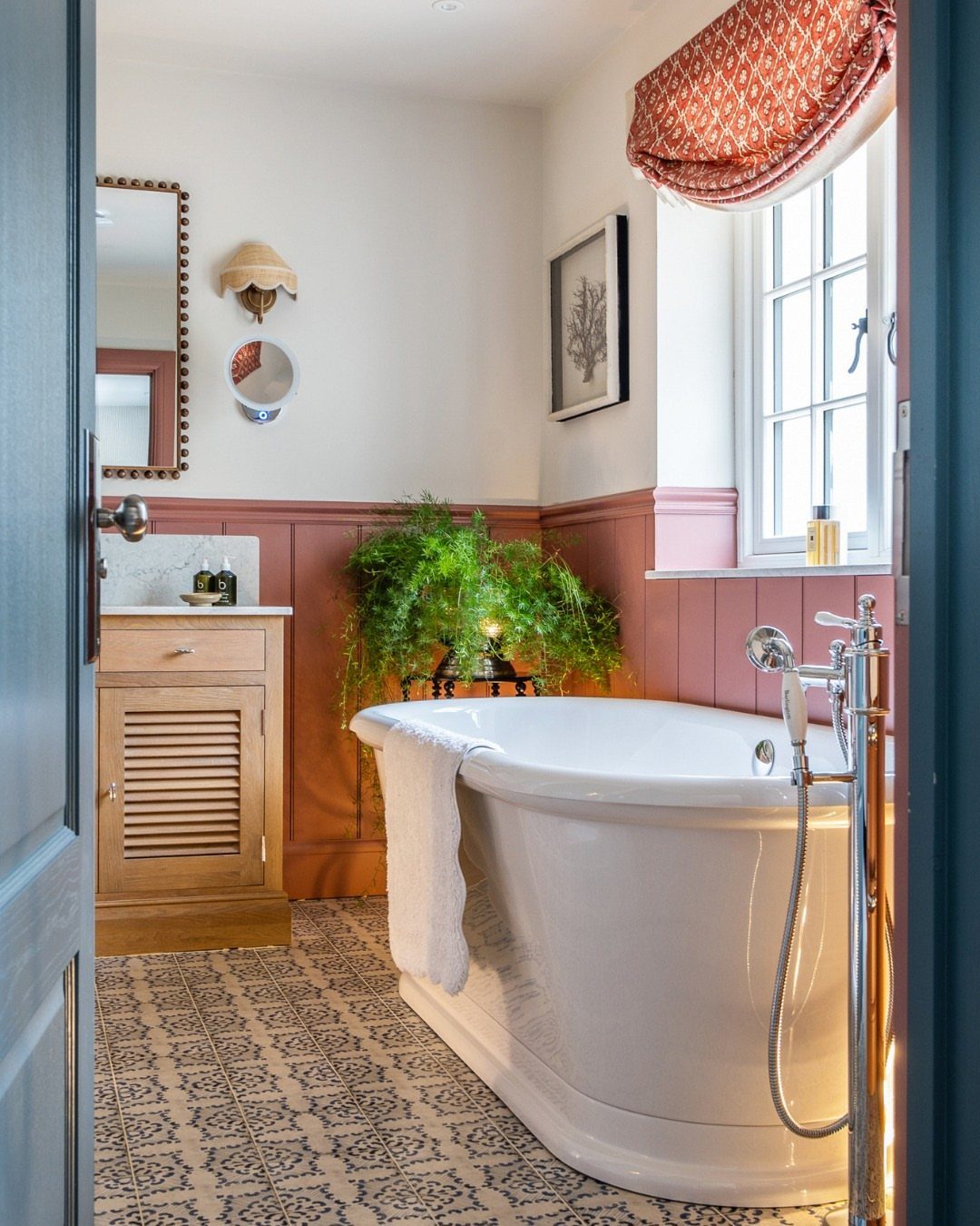 White freestanding bathtub in a small bathroom with patterned floor tiles and pink paneling.