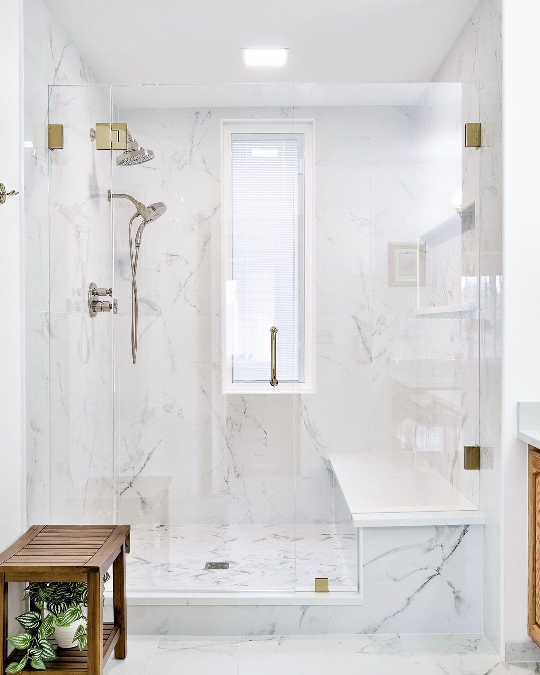 Clear glass shower panels enclosing a white marble shower with a built-in bench.