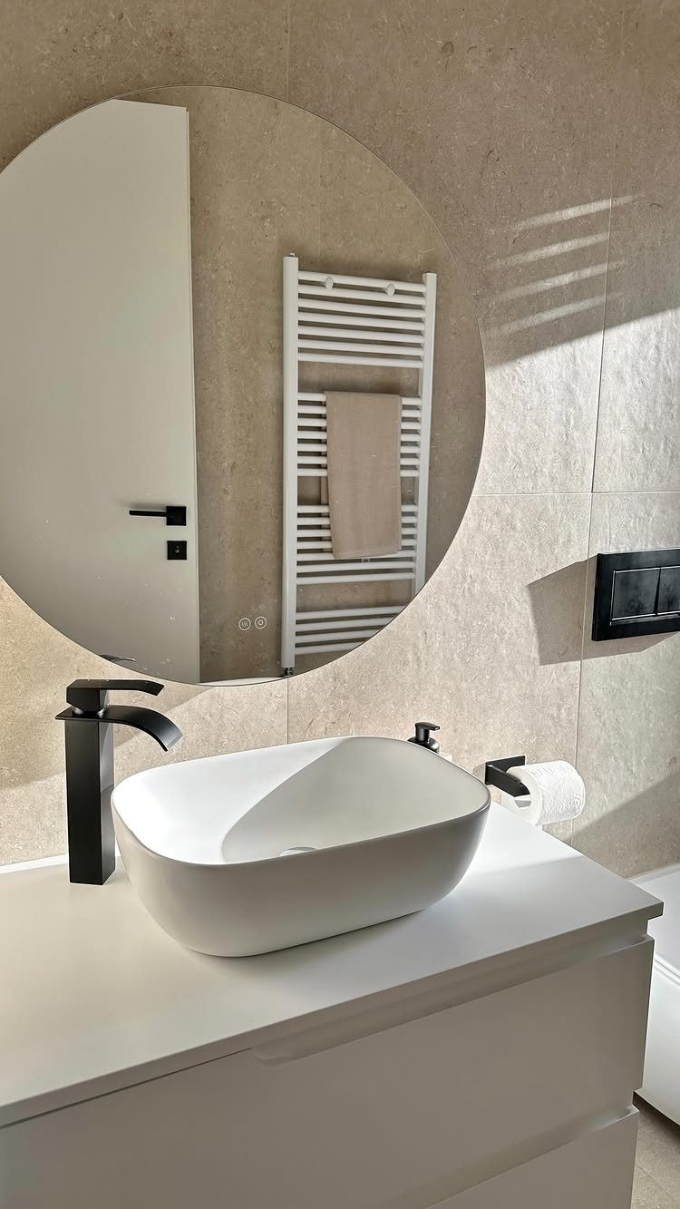 White vessel sink and vanity with a large circular mirror and beige tiles.