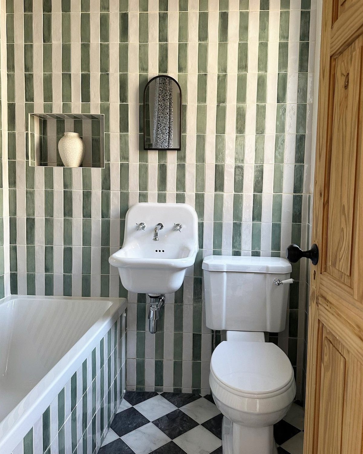 Long narrow green and white vertical tiles in a small bathroom with white fixtures.