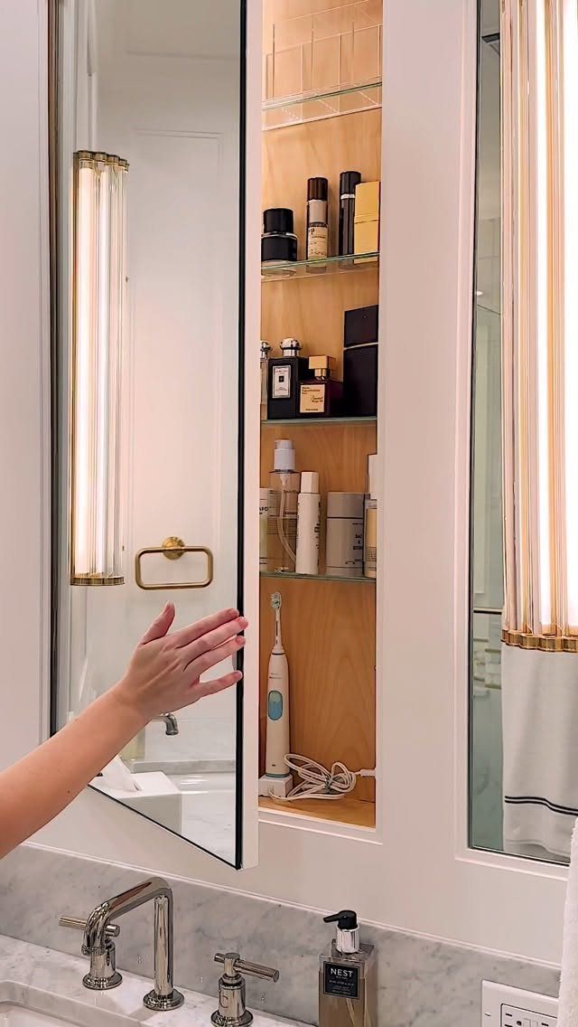 Mirrored bathroom cabinet open to reveal wooden shelves with skincare and toiletries.