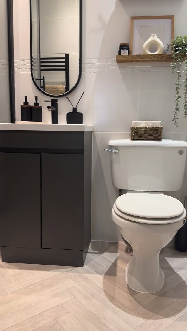 Narrow black-framed oval mirror above a dark grey vanity in a small bathroom.