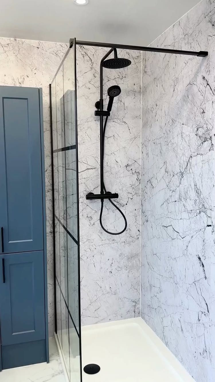 White marble wall panels in a shower with black fixtures and glass door.