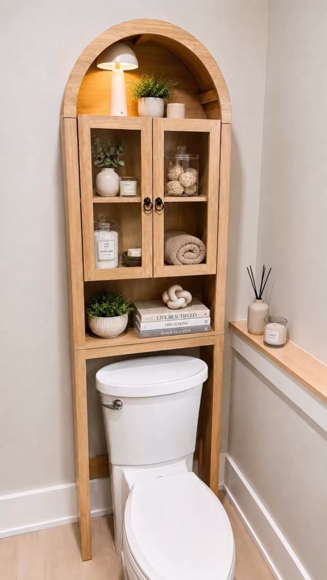 Wooden storage cabinet with glass doors and arched top installed over a white toilet.