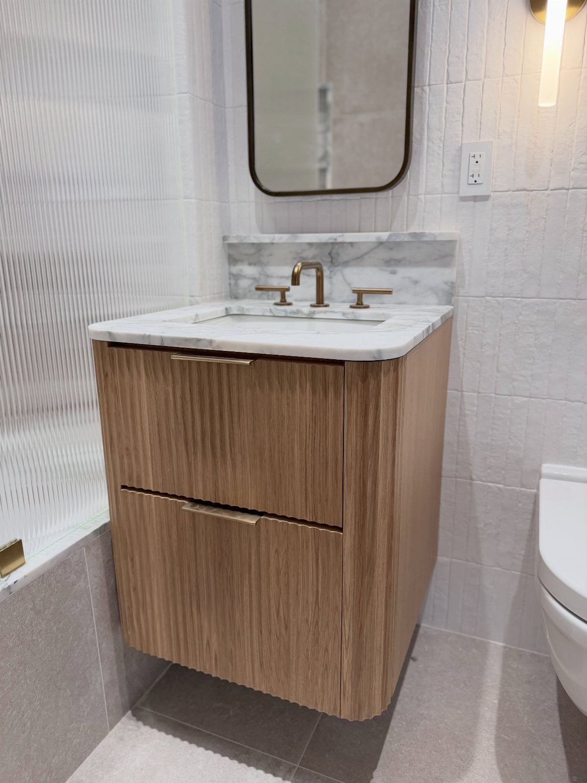 Wooden bathroom vanity with marble top and gold faucet in a small space.