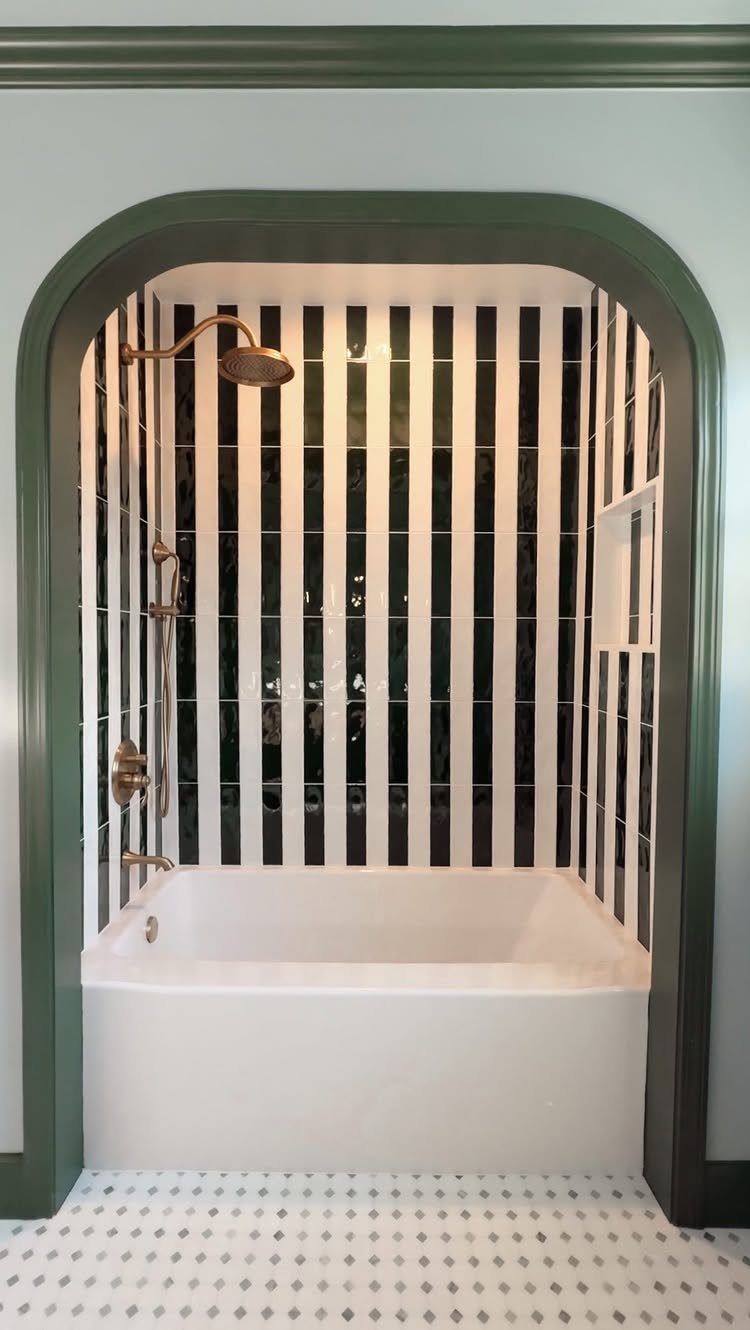 White bathtub and shower with black and white striped tiles in an arched alcove