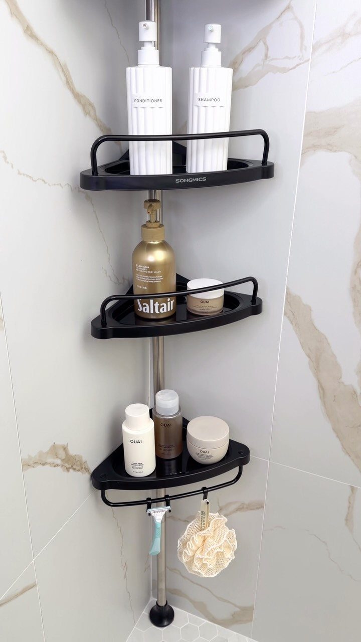 Black three-tier corner shower caddy with toiletries against white marble wall tiles.