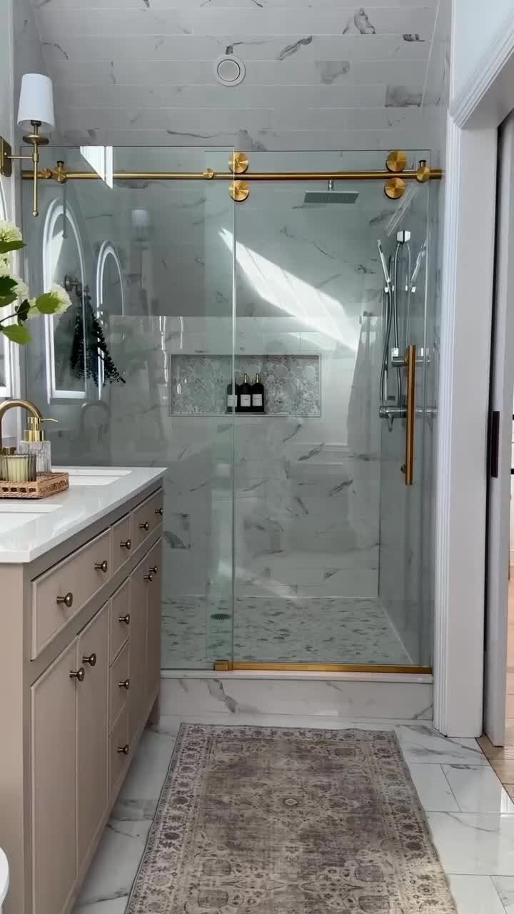 Glass shower enclosure with gold sliding doors in a white marble bathroom.