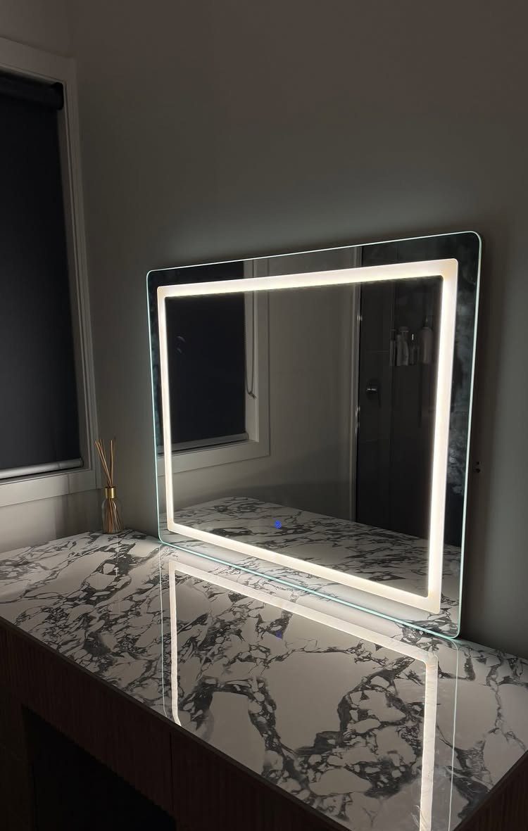 Rectangular bathroom mirror with an illuminated LED border above a marbled vanity countertop.