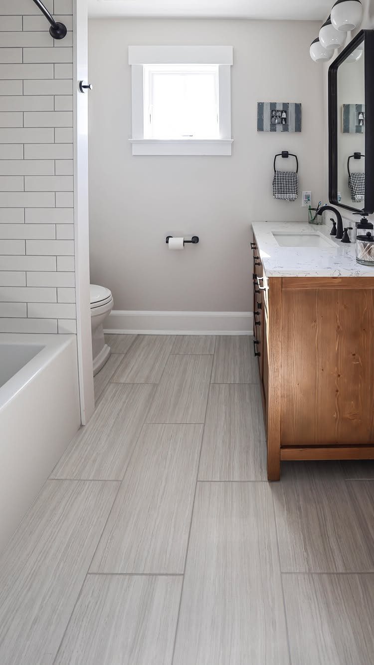 White subway wall tiles in a bright bathroom with a wooden vanity and grey flooring.