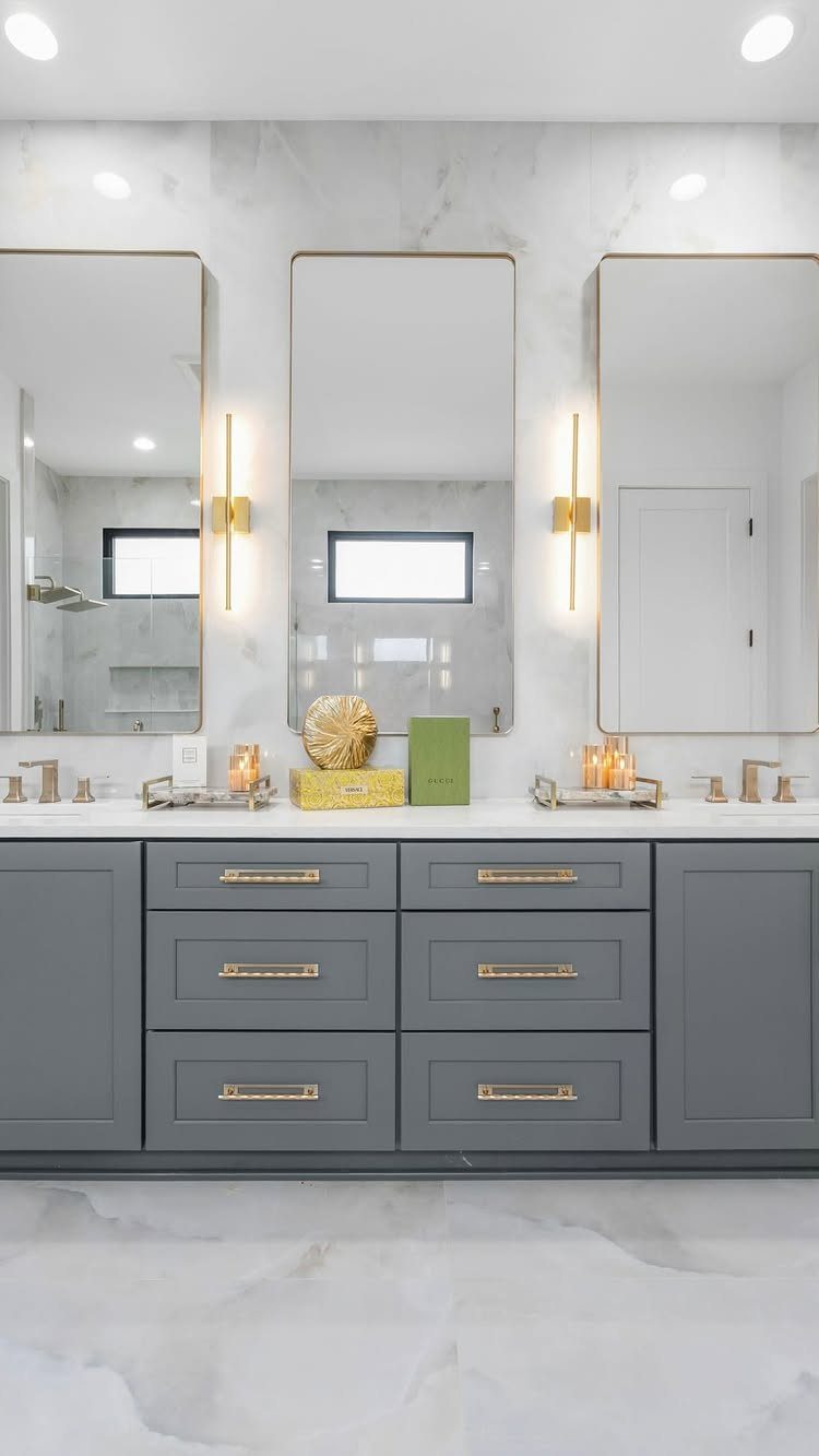 Grey bathroom vanity with white marble countertop and three gold-framed mirrors.