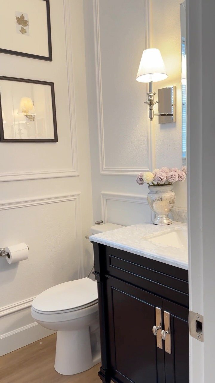 Wall-mounted lamp with white shade illuminating a dark wood bathroom vanity