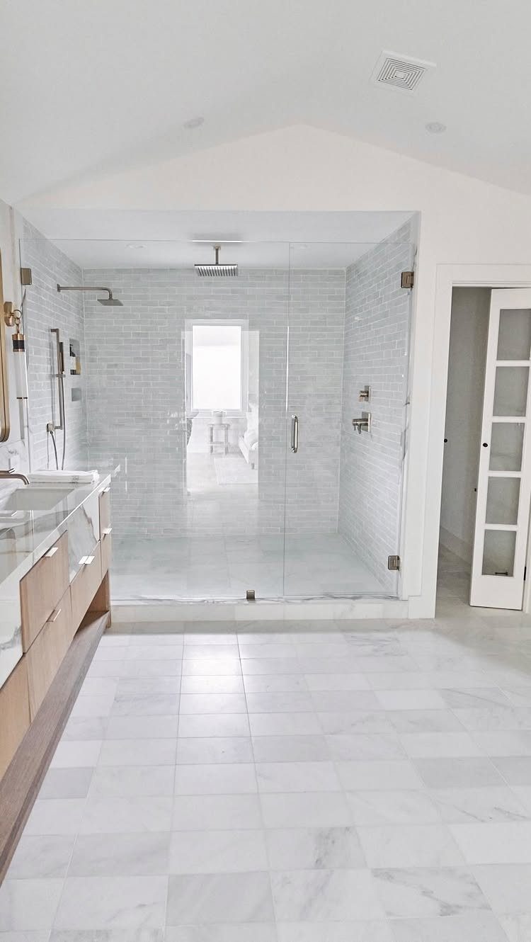Glass-enclosed walk-in shower with white tiles and marble flooring in a modern bathroom.