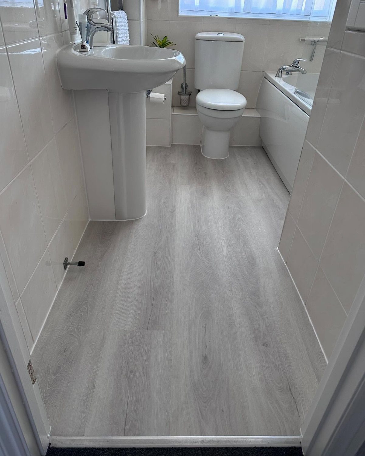Grey wood-look vinyl flooring in a white bathroom with sink and toilet