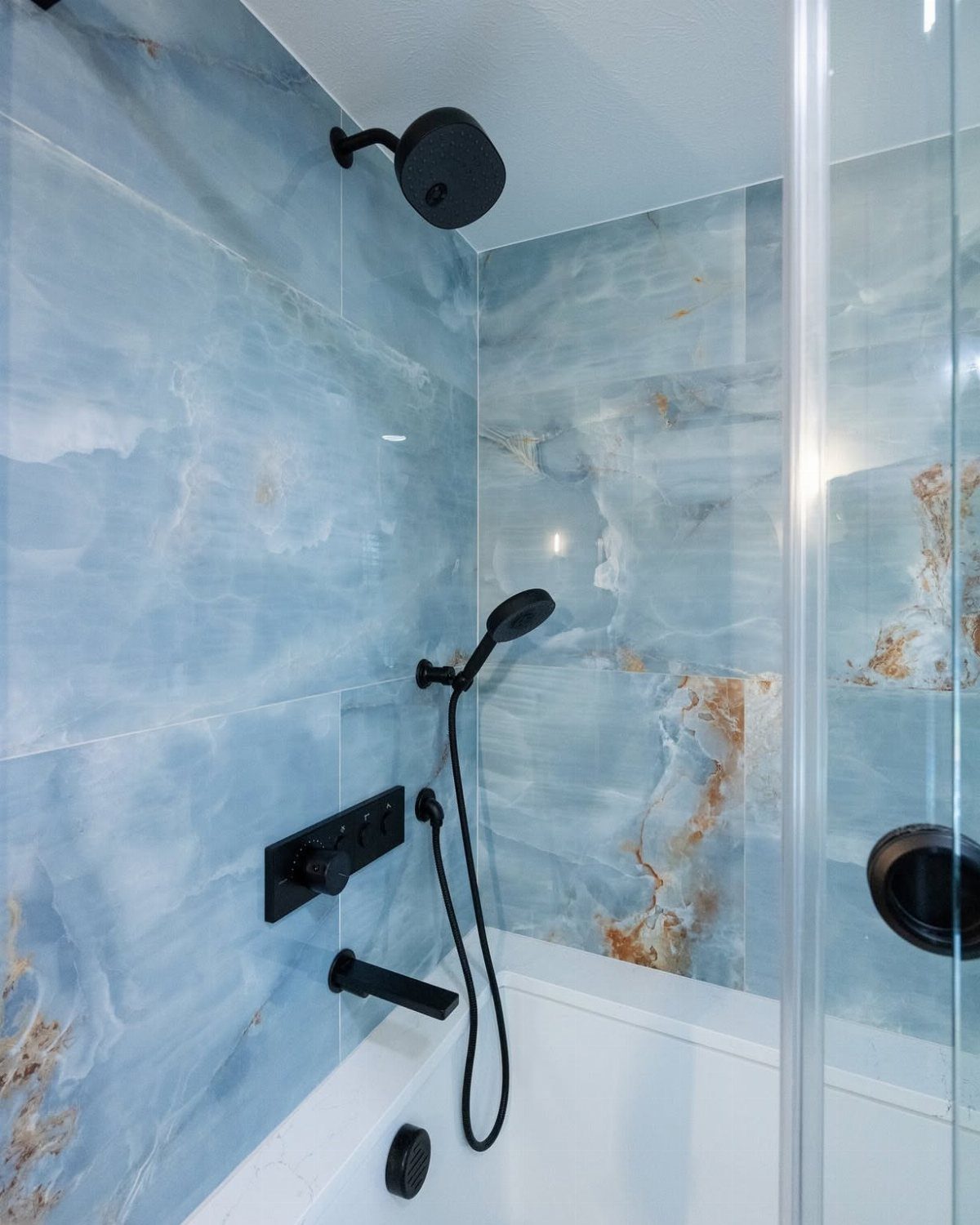 White bathtub with black fixtures against marbled blue tile accent walls