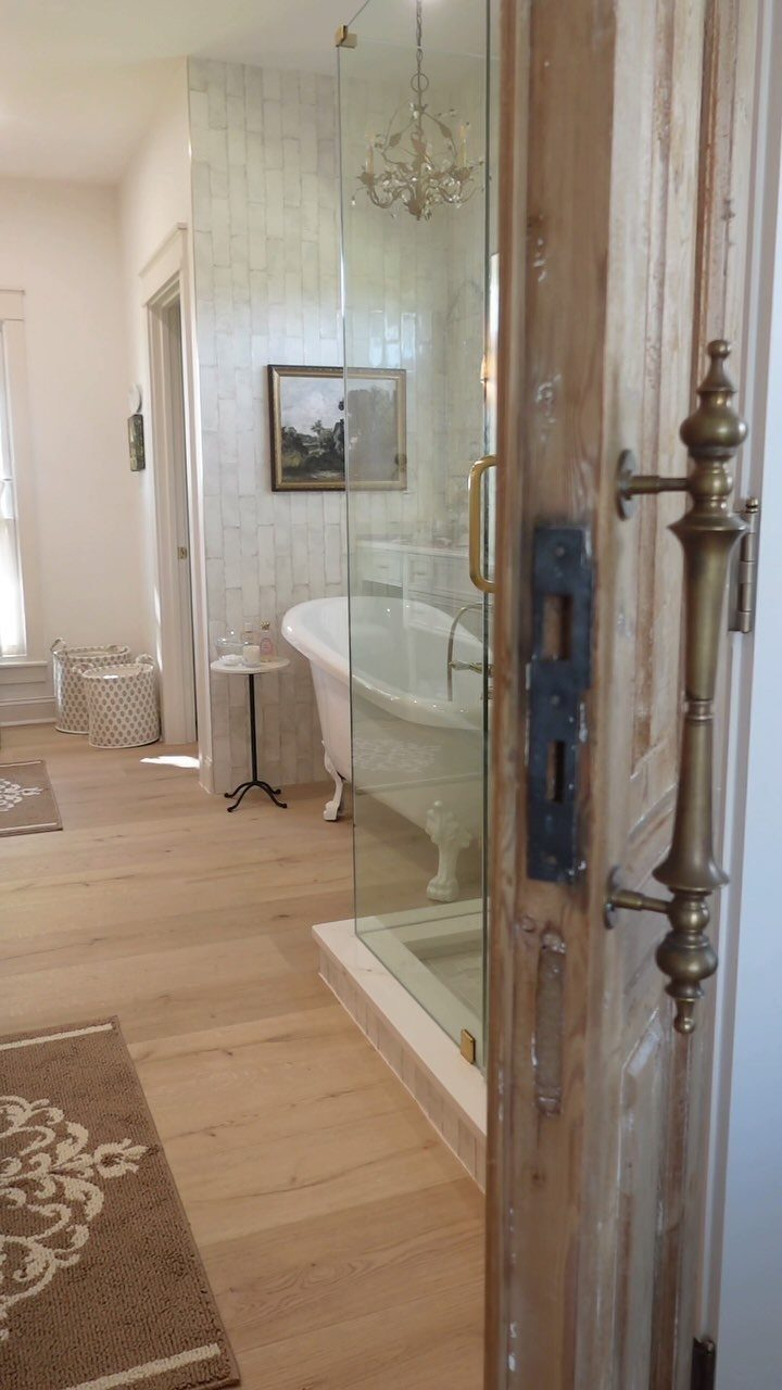 White claw-foot bathtub in a bright bathroom with light wood floors and tiled walls.