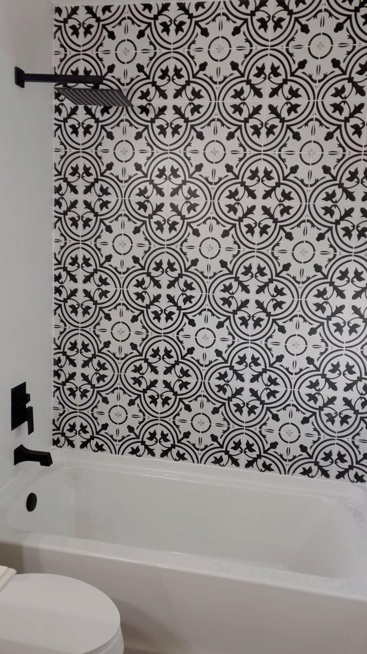 White bathtub and shower with black fixtures against patterned black and white tiles.