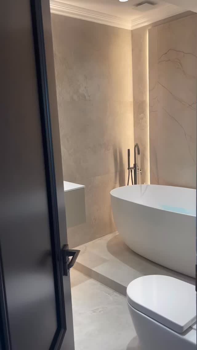 White freestanding bathtub with black fixtures in a beige stone bathroom.