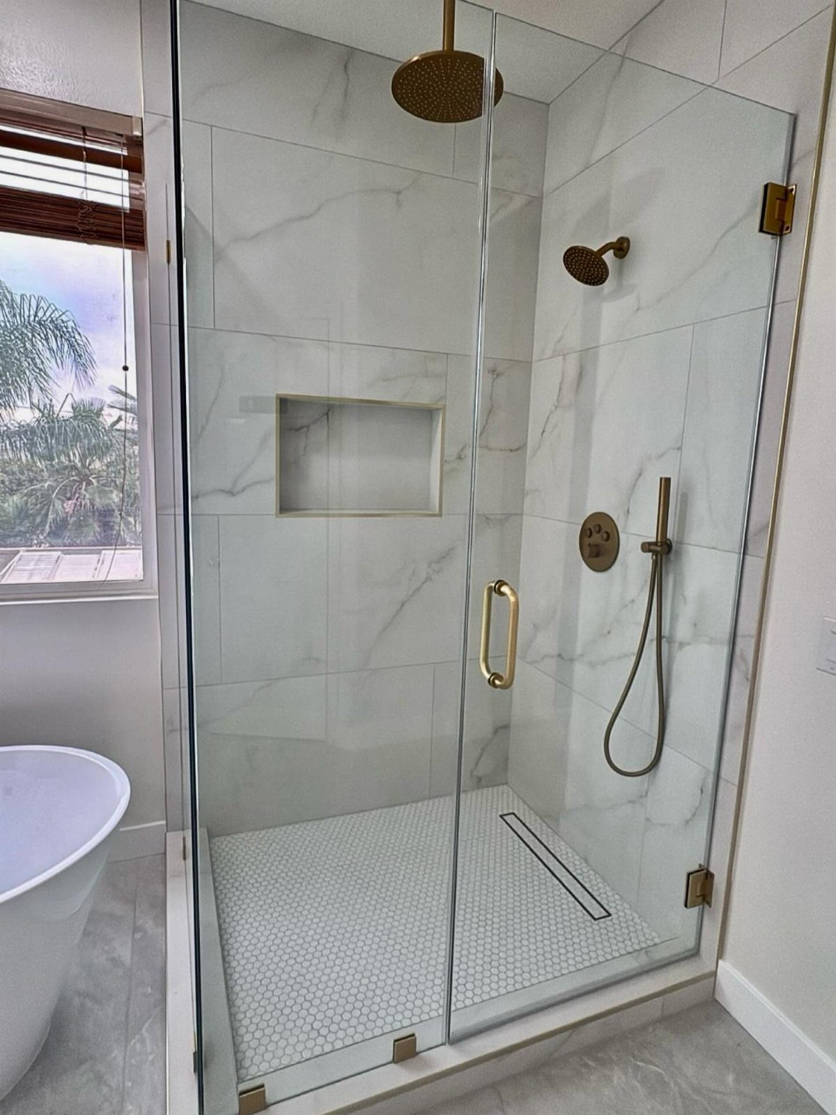 Modern shower with white marble tiles, gold fixtures, and a linear floor drain.