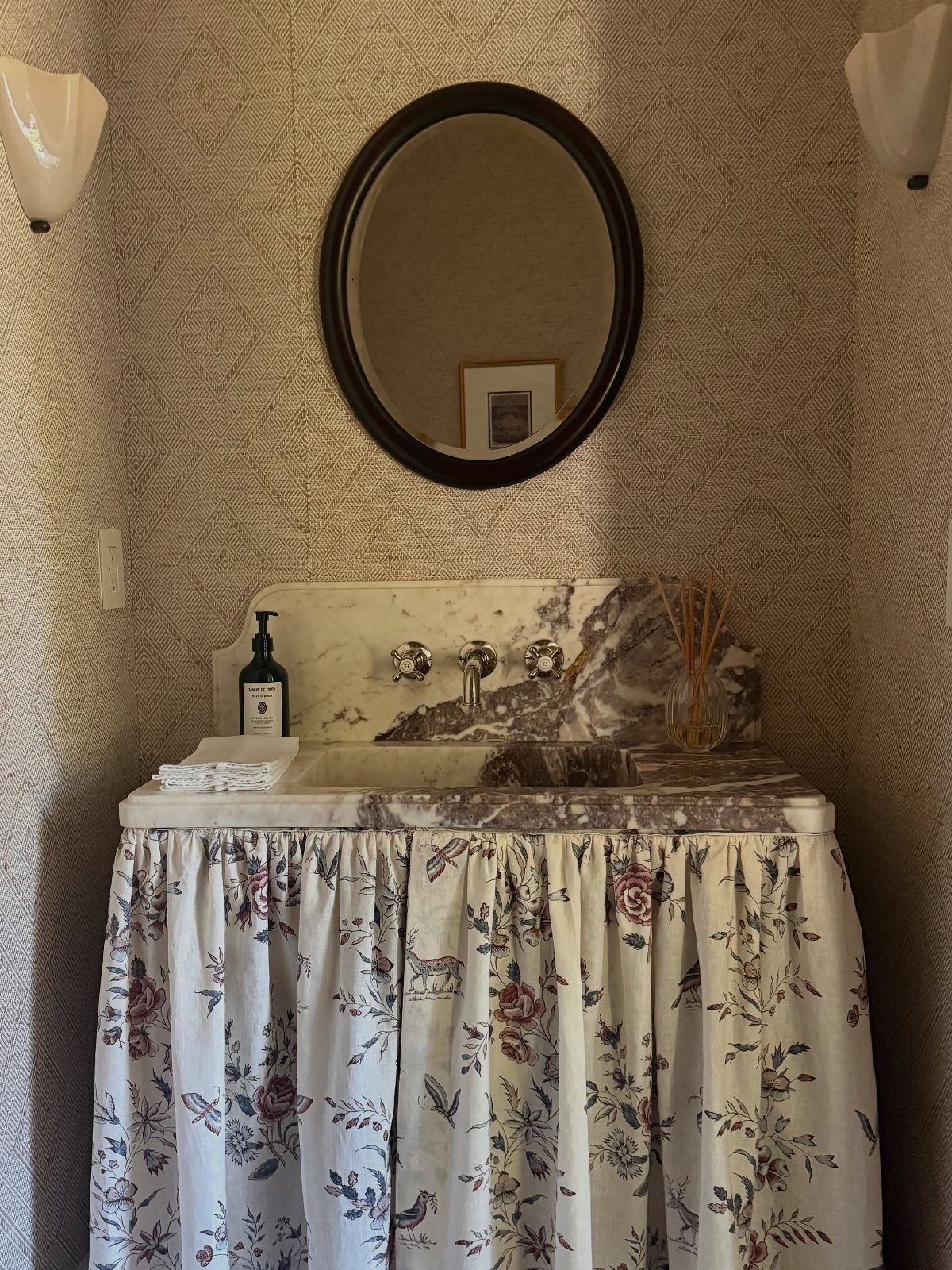 Marble sink with a white floral fabric skirt and round black mirror above