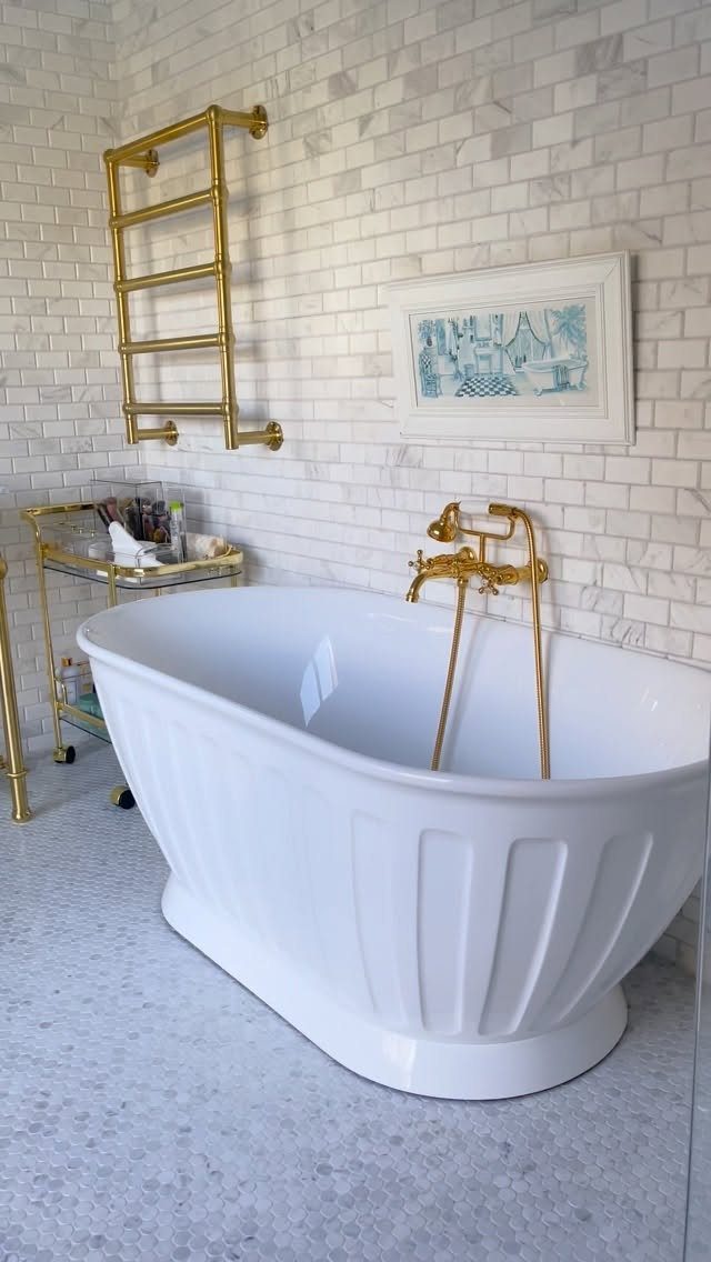 Gold rolling storage cart next to a white freestanding bathtub with gold fixtures.