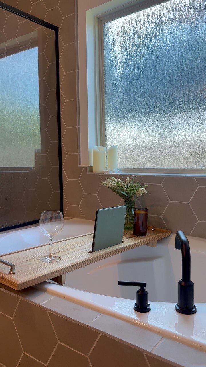 Wooden tub tray with wine glass and tablet across a white bathtub