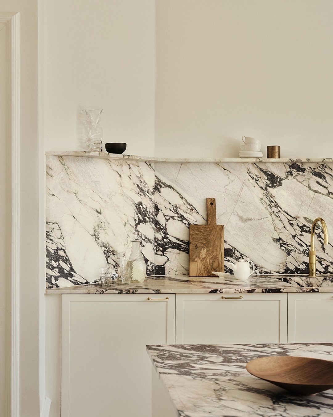 Marbled stone kitchen backsplash and countertop with off-white cabinets and gold hardware.