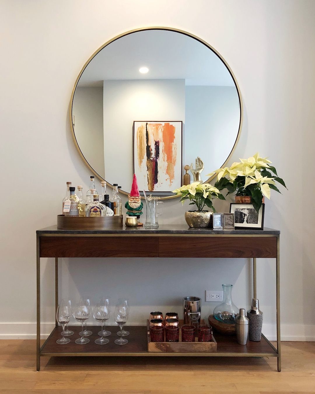 Barware on a gold tray atop a wooden console table with a round mirror.