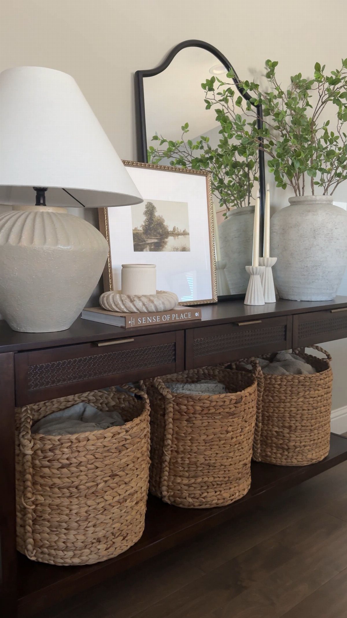 Woven wicker baskets stored on the lower shelf of a dark wood console table.
