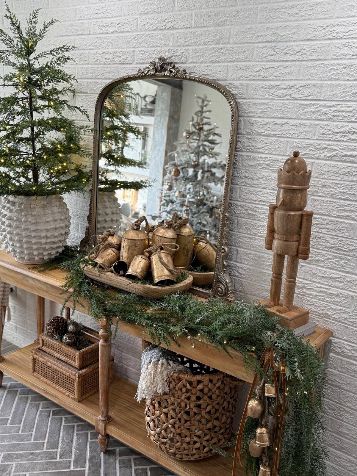 Wooden console table decorated with evergreen garland, gold bells, and a nutcracker figurine.