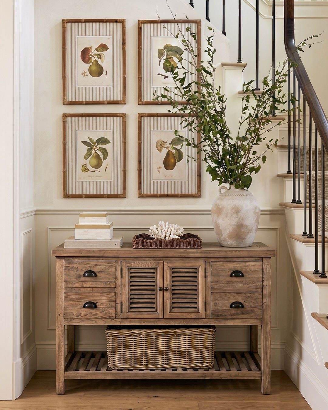 Wooden console table with drawers and a wicker basket under a botanical art gallery.