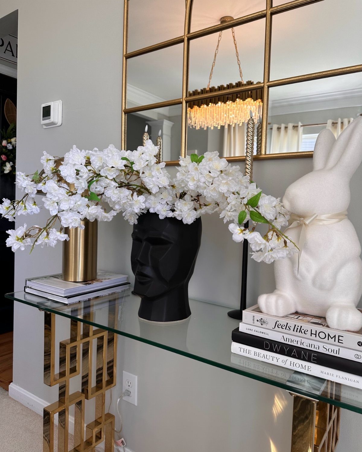 White blossoms in a black head-shaped vase on a glass console table.