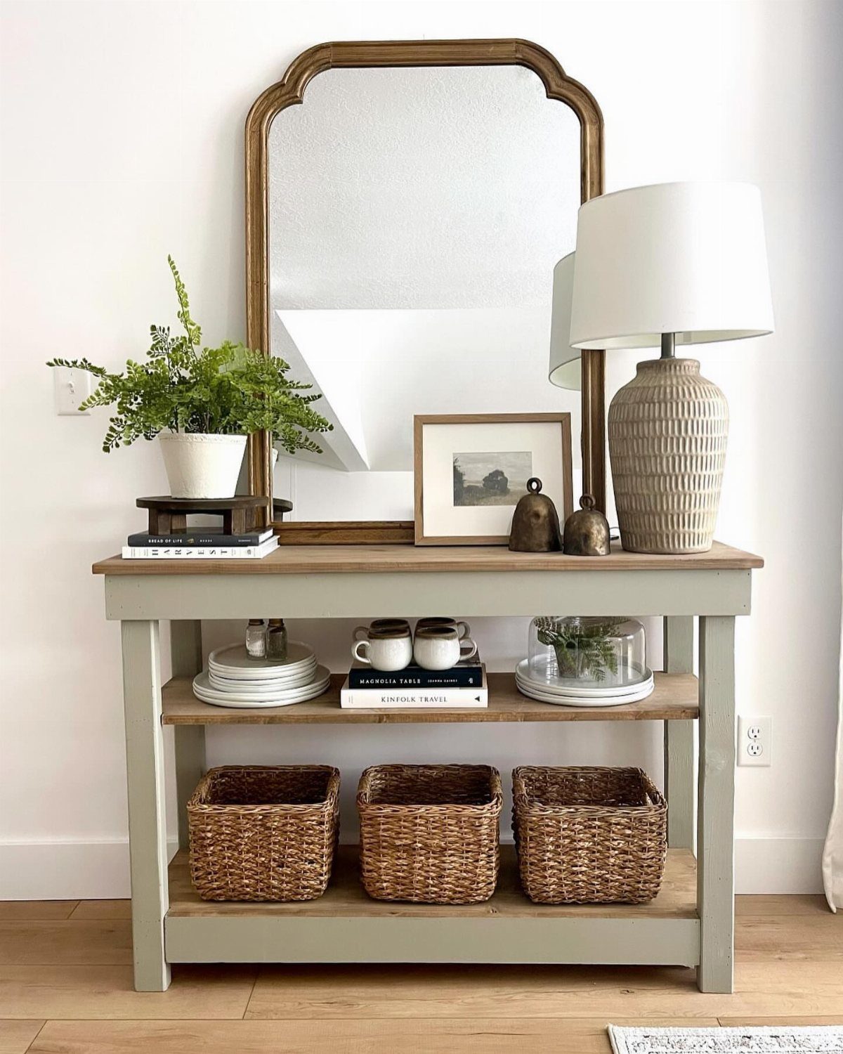 Wooden console table with a mirror, lamp, and woven baskets on a lower shelf.