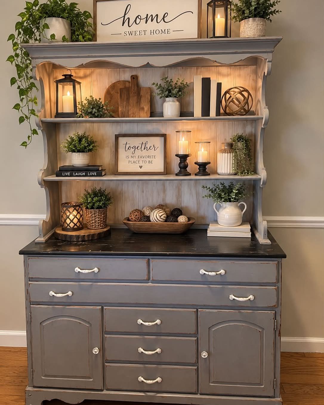 12 Dining Room Decor Hutch Ideas, From Farmhouse to Japandi 2 Grey wooden hutch decorated with greenery, lanterns, and rustic home decor signs.