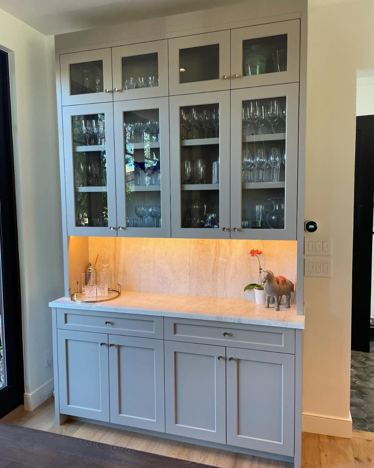 12 Dining Room Decor Hutch Ideas, From Farmhouse to Japandi 5 Light grey built-in hutch with glass cabinets, marble countertop, and warm under-cabinet lighting.
