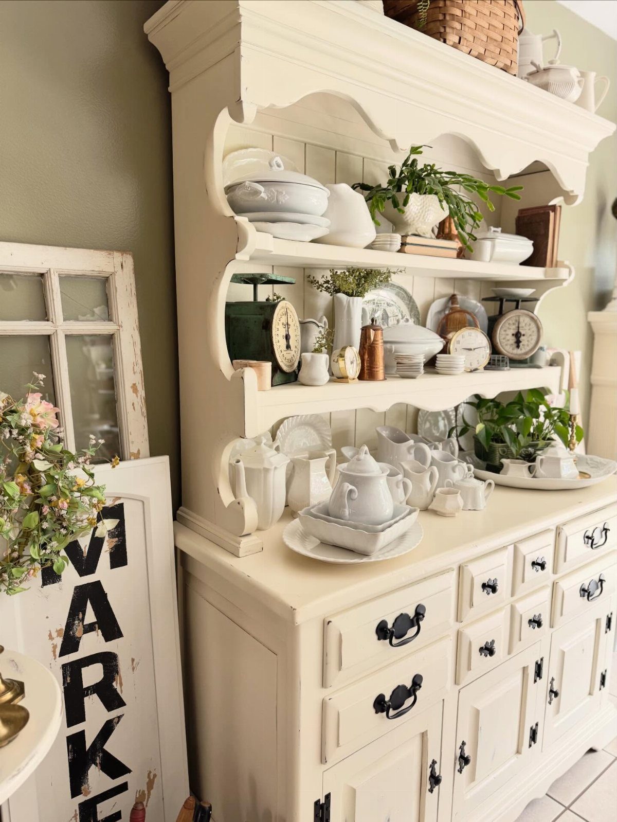12 Dining Room Decor Hutch Ideas, From Farmhouse to Japandi 9 Cream vintage hutch filled with white ceramic dishes and a small green plant.