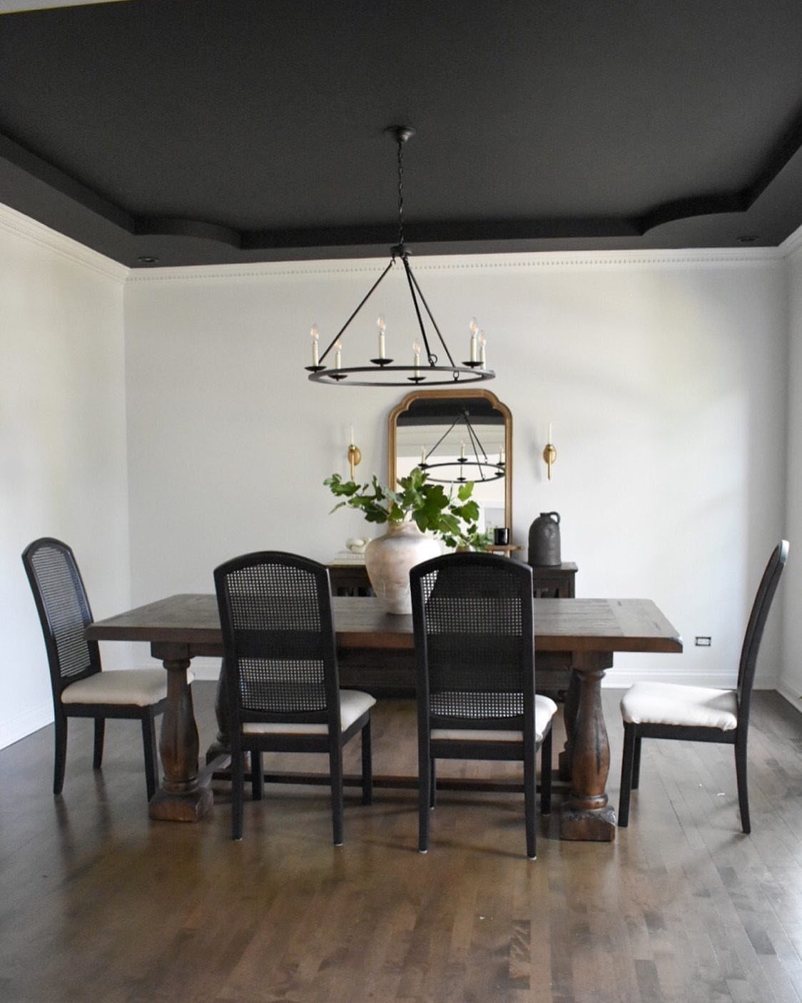 Dining room with a matte black ceiling, wooden table, and black cane-back chairs.
