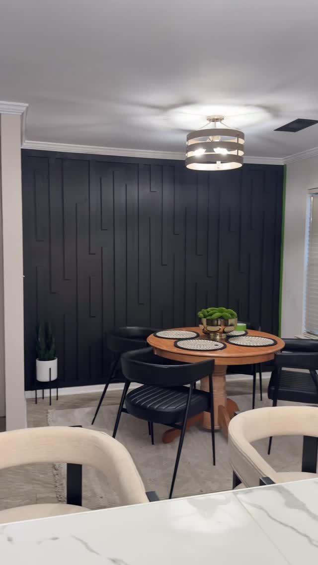 Black paneled accent wall in a dining room with a round wooden table.