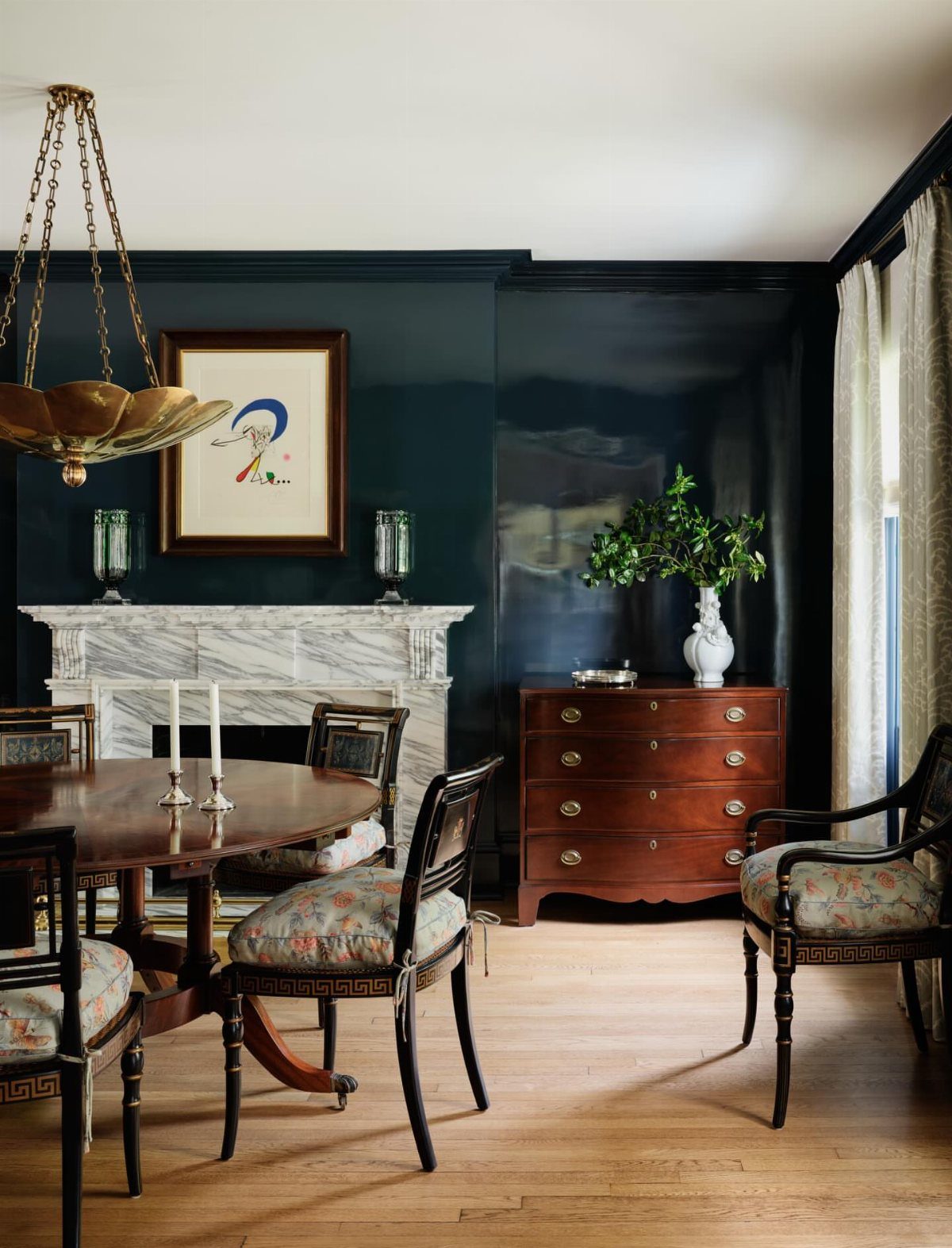 Dark blue walls in a dining room with a marble fireplace and wood furniture.