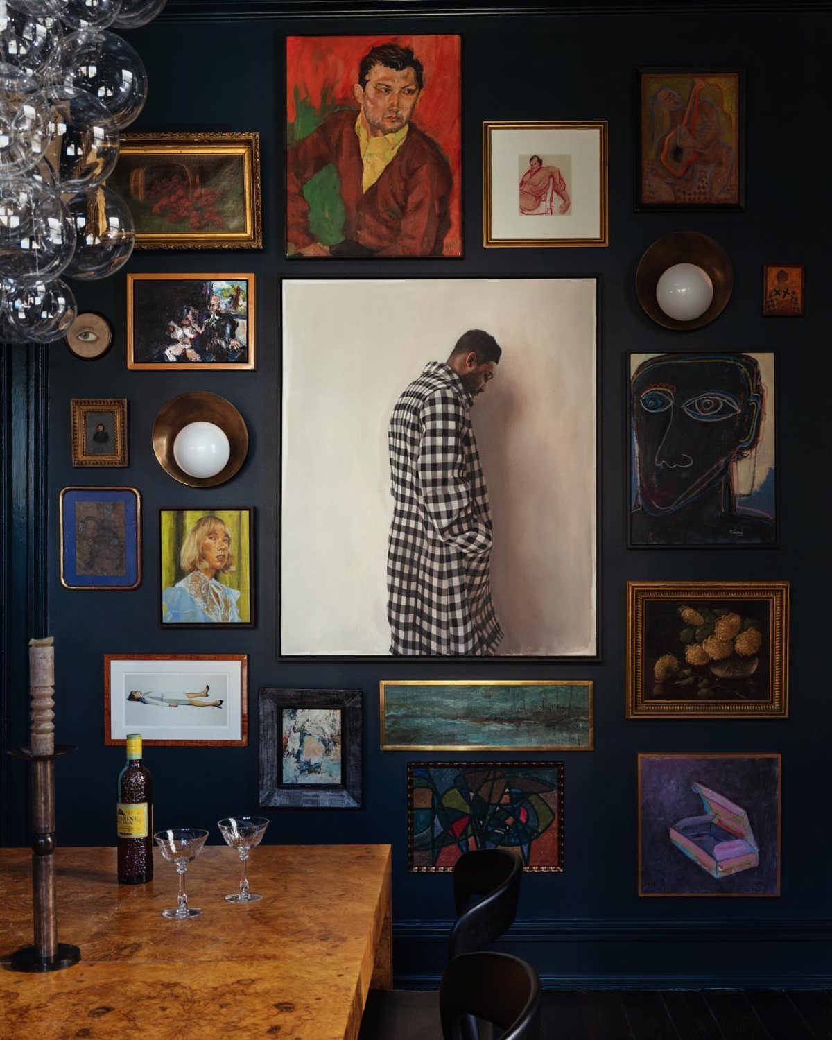 Gallery wall of dark-hued oil paintings on a deep blue dining room wall.