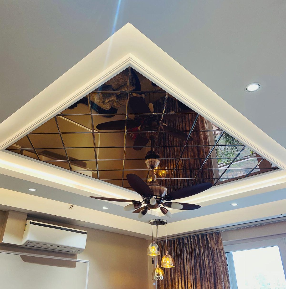 Mirrored ceiling panels in a recessed square frame reflecting a ceiling fan and lights