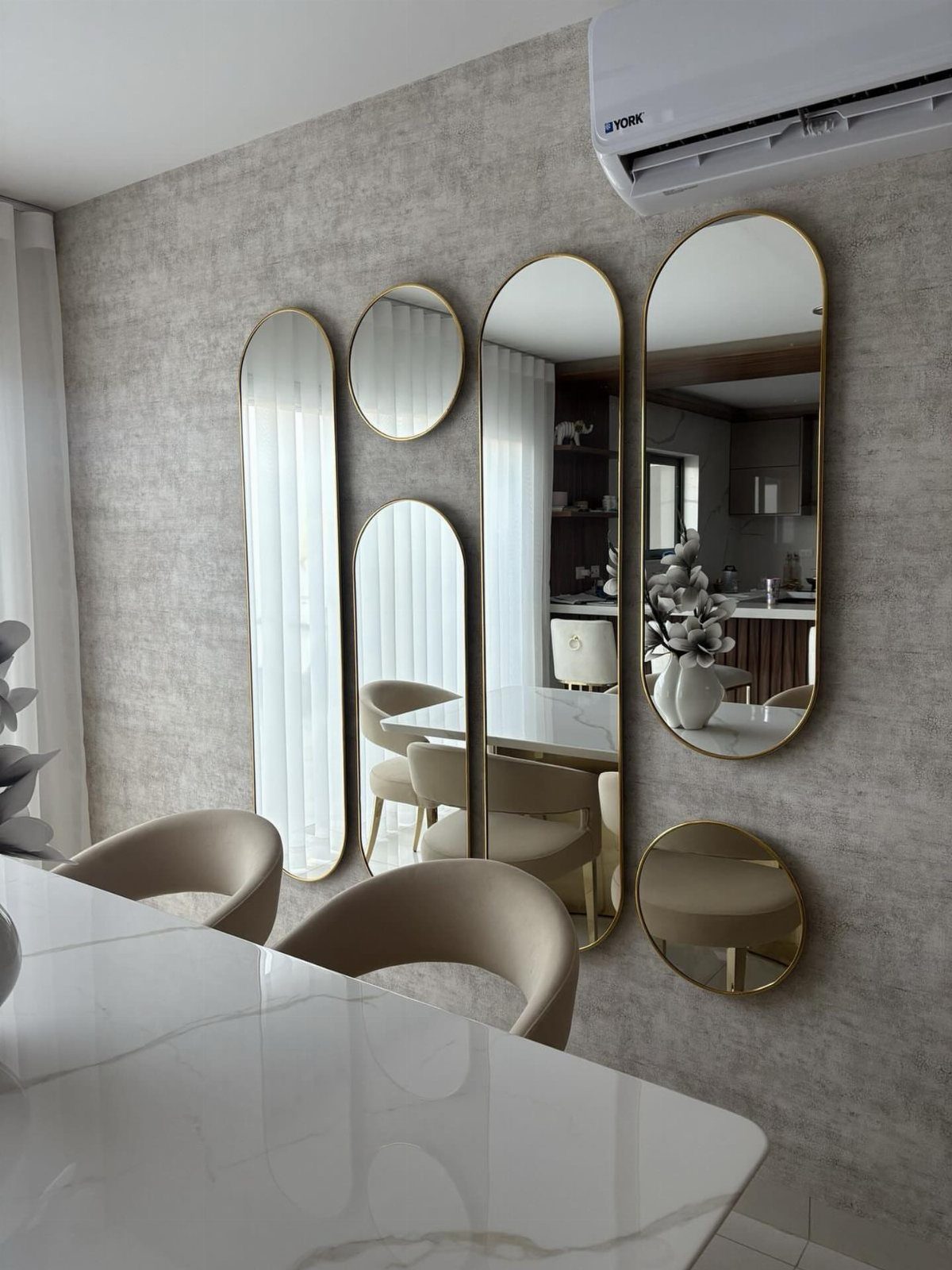 Gold-framed mirrors of various shapes mounted on a grey wall in a dining room.