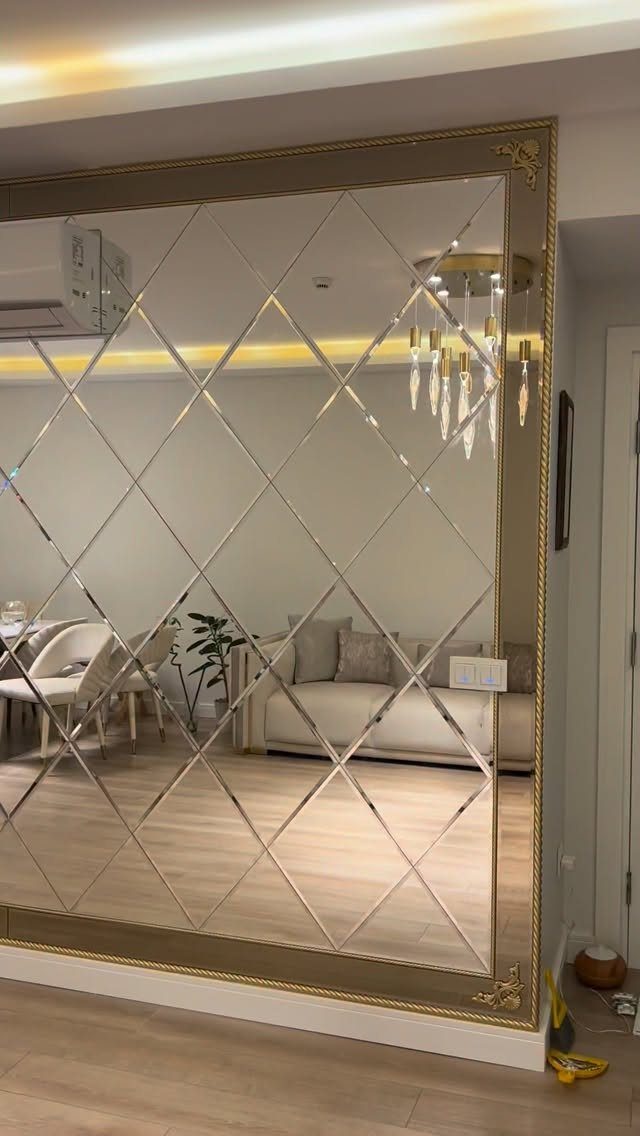 Gold-framed wall mirror with diamond beveled patterns reflecting a modern living room interior.