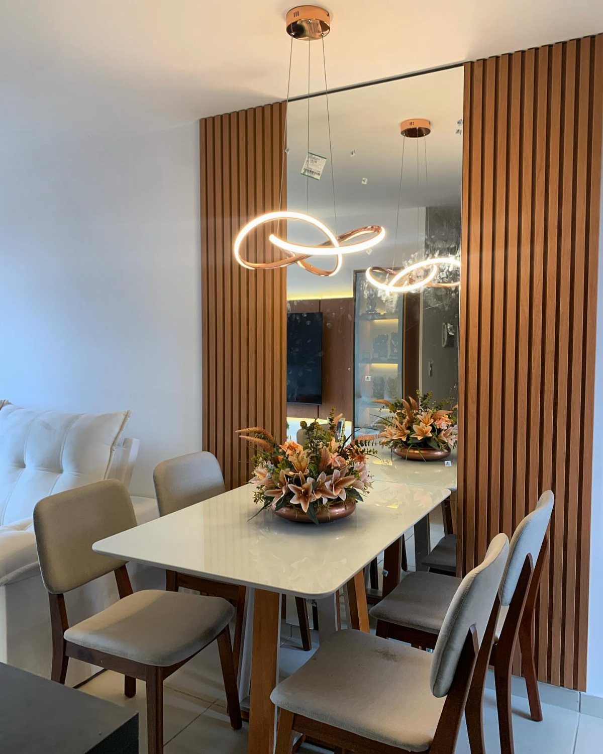 White marble dining table with beige chairs and a large recessed wall mirror.