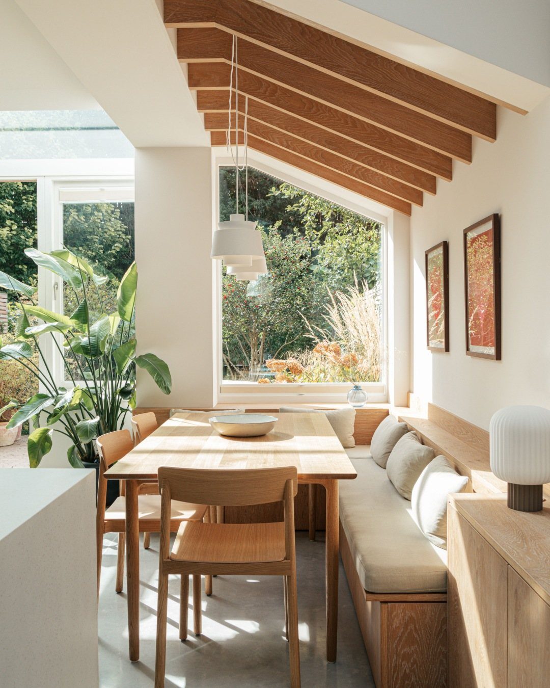 Dining nook with wooden ceiling beams, light wood furniture, and a large window.
