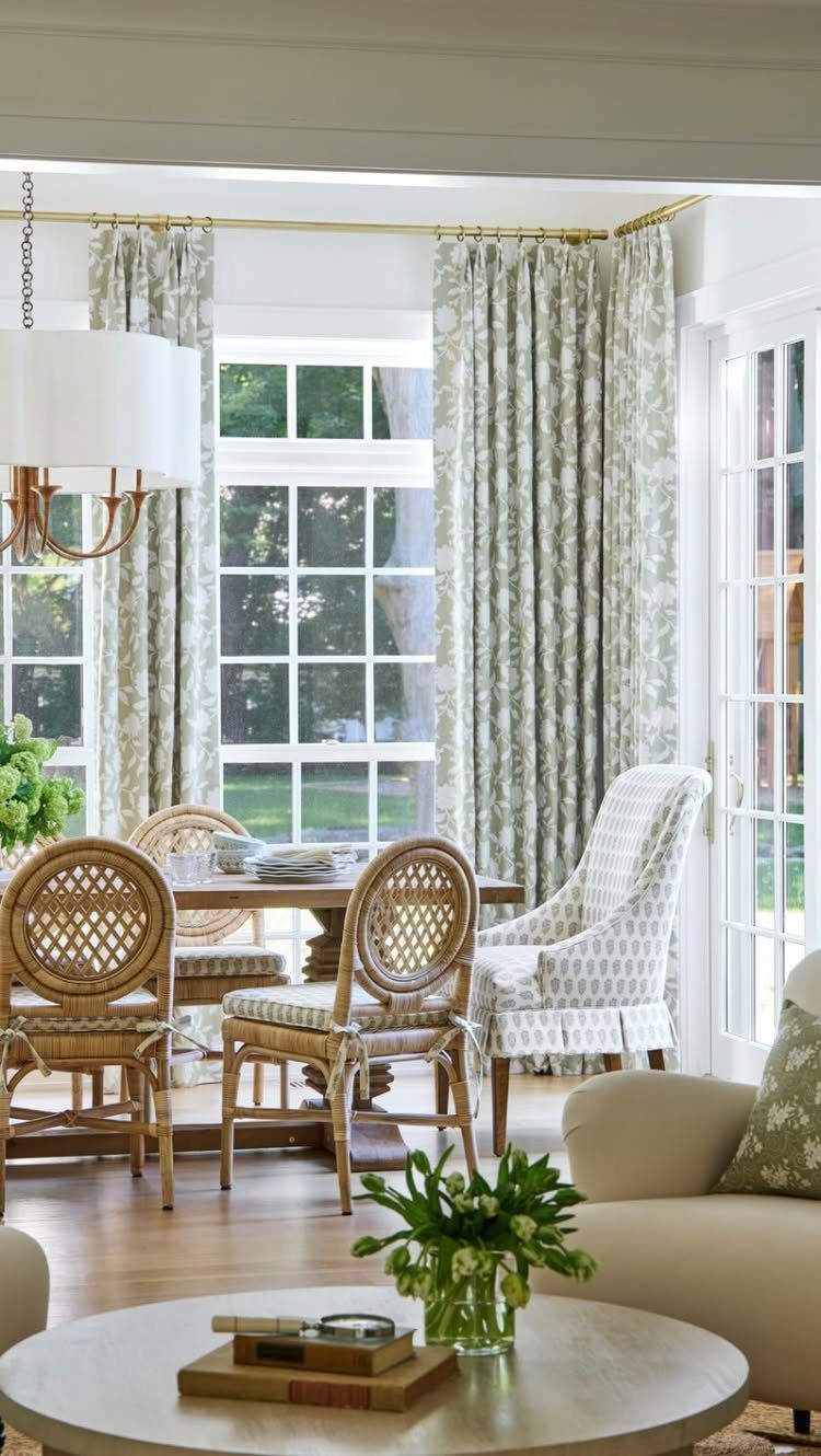 Dining area with wooden table, woven bistro chairs, and floral green curtains.